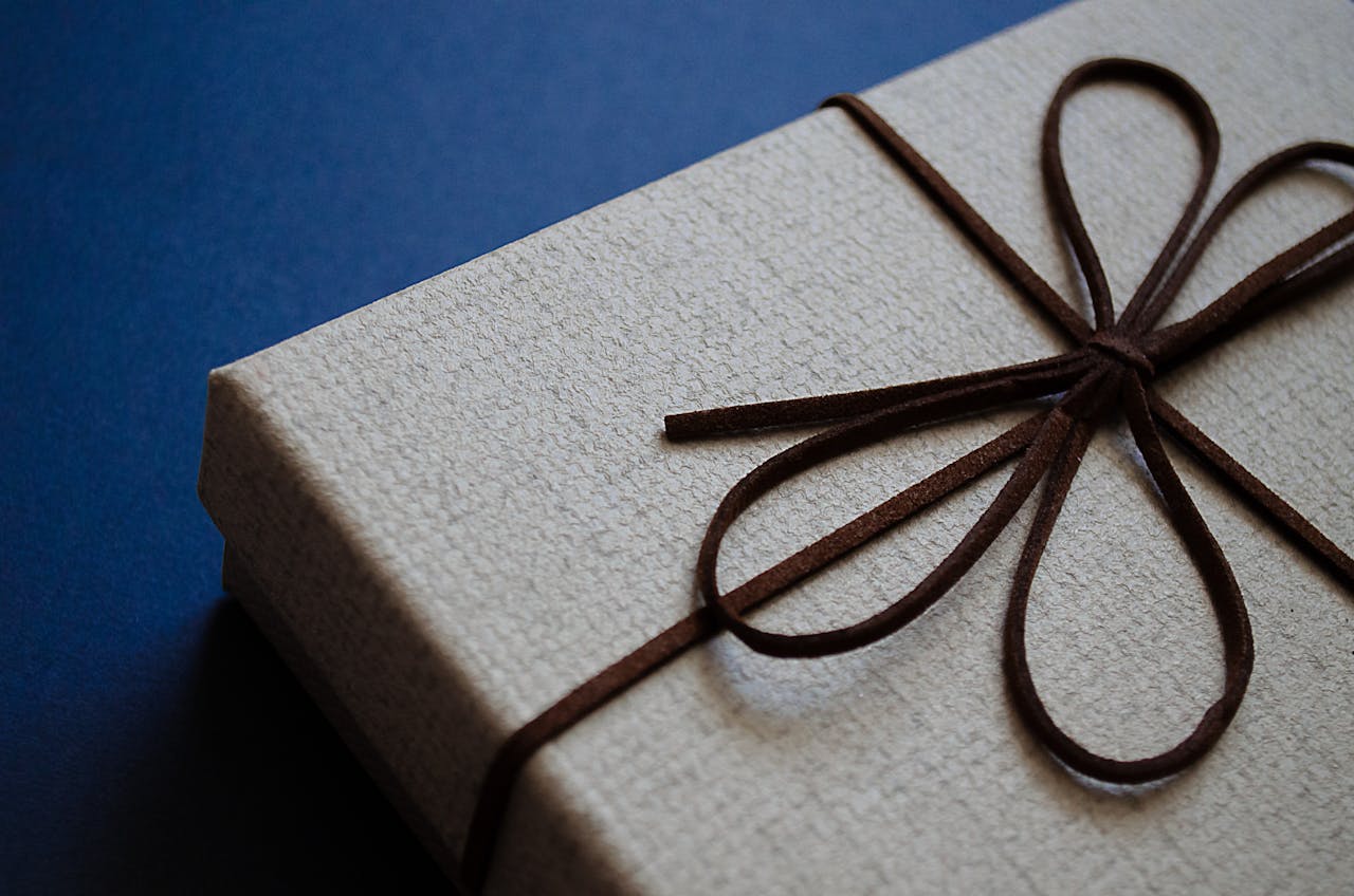 Close-up of an elegant gift box with a brown leather bow on a blue surface, perfect for special occasions.